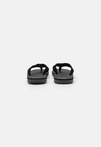 Chaussons noirs avec des sangles en tissu texturé et une semelle grise rembourrée. Présente un design simple, un bout ouvert et un talon plat.