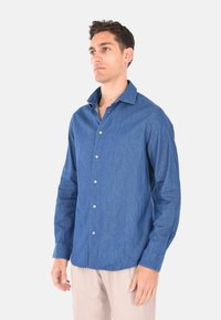 Camicia in denim di blu medio, con design a bottoni, maniche lunghe, colletto a punta, bottoni bianchi e una texture liscia e leggera.