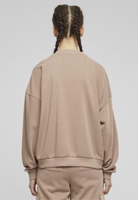 Felpa beige oversize con spalle scese, polsini e orlo a costine. Texture morbida, design semplice, senza marchi o motivi visibili.