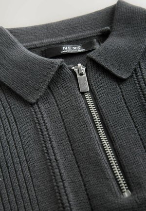 Tamsiai pilkas megztas polo megztinis su apykakle ir priekinės pusės užtrauktuku. Yra vertikalus nėrčių raštas ir sidabrinis užtrauktukas.