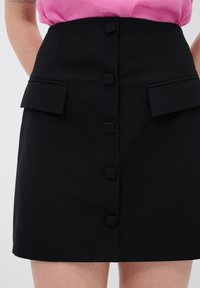 Zwarte rok met een aansluitende taille, voorzien van vijf vierkante knopen aan de voorkant, twee zijzakken en een gladde textuur.
