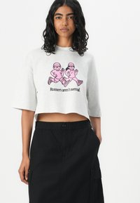 Grå kort sweatshirt med rosa grafikk av to løpere og teksten "Løpere er ikke normale." Kombinert med svarte høyt midjede cargo-shorts.