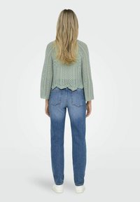 Maglione in verde menta lavorato a maglia con orlo a scallop e motivo in pizzo, abbinato a jeans blu a vita alta e sneakers bianche.