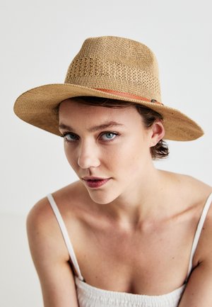 Prútený slamenný klobúk vo svetlej béžovej farbe s širokým okrajom a úzkym hnedým koženým pásikom. Textúrovaný povrch s detailnými tkanými vzormi.