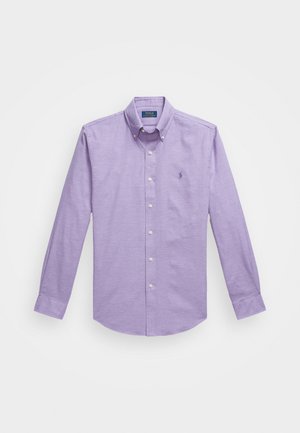 Chemise à manches longues, boutonnée, en tissu violet clair, avec un col classique et un petit logo brodé sur le côté gauche de la poitrine.