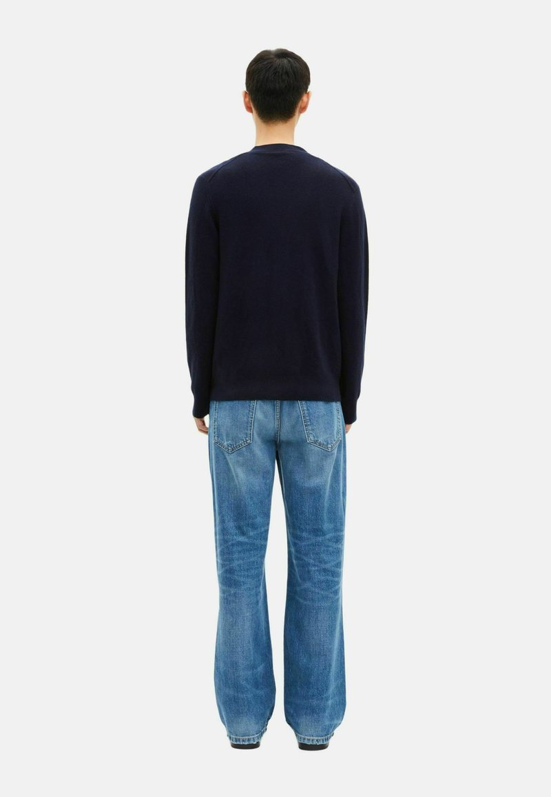 Navy sweater, textured fabric, crew neckline. Light blue wide-leg jeans with back pockets and faded denim finish. Model facing away.