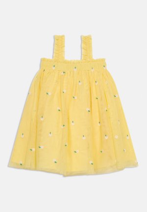 Κίτρινο αμάνικο φόρεμα με βολάν στα τιράντες και μικρή λευκή και πράσινη κεντητή floral διακόσμηση διάσπαρτη στο ύφασμα.