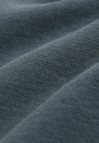 Grau Baumwollstoff mit feiner Stricktextur, der glatte, weiche Falten und einen leichten Glanz zeigt. Keine deutlichen Muster oder Akzente.