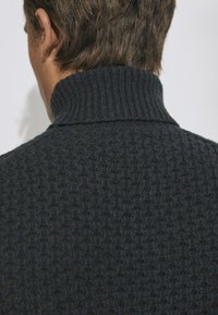 Ciemny sweter dziergany, z wysokim prążkowanym kołnierzem, teksturowaną tkaniną z wzorem w kratę i dopasowanym krojem.