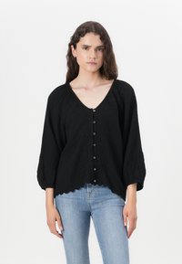 Black blouse in lightweight fabric, featuring a deep V-neck, embroidered floral pattern, button closure, and puffed sleeves with scalloped hem.