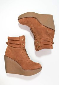 Brązowe zamszowe botki na koturnie z wysoką, teksturowaną podeszwą platformową, wiązane z przodu oraz ze ściągaczem przy mankiecie ozdobionym złotymi akcentami.