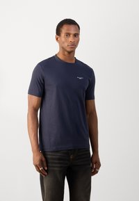 Navyblauwe katoenen T-shirt met korte mouwen, ronde hals en klein wit logo op de linkerborst. Soepele textuur, casual pasvorm.