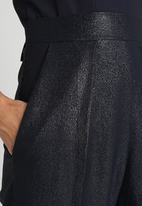 Námořnické modré plisé kalhoty s hladkým, lesklým povrchem, se štíhlým pasem a bočními kapsami pro funkčnost.