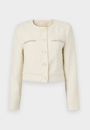 Veste blanche courte en tissu texturé, col rond, cinq boutons et accents en cristal sur les poches poitrine.