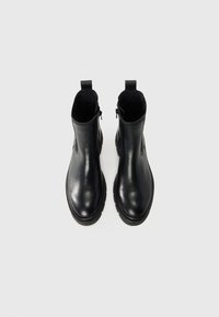 Botas de tobillo de cuero negro con un acabado liso, paneles elásticos en los laterales y una suela de goma texturizada. Cierre de cremallera a cada lado.