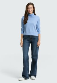 Lichtblauwe coltrui met lange mouwen, gecombineerd met donkerblauwe flared jeans en witte sneakers. Zachte textuur, casual pasvorm.