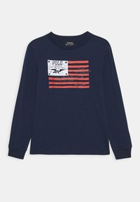 Laivansinis pitkähiha shirt, jossa on punaisia raitoja ja valkoinen suorakulmainen graafinen kuva, jossa on tekstiä ja tähtiä rinnan kohdalla.