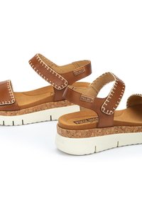 Sandalias de cuero marrón con suelas de plataforma de corcho, suelas exteriores de goma blanca y detalle de costura en las correas. Correas ajustables para un ajuste seguro.