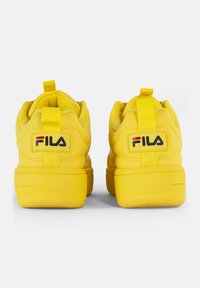 Gule joggesko med en glatt syntetisk overdel, polstret krage og teksturert såle. Har en pull-tab og svart FILA-logo på hælen.