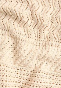 Tela de textura cremosa con un patrón de zigzag, que presenta secciones de tejido abierto y una apariencia suave y de punto. Ideal para aplicaciones acogedoras.