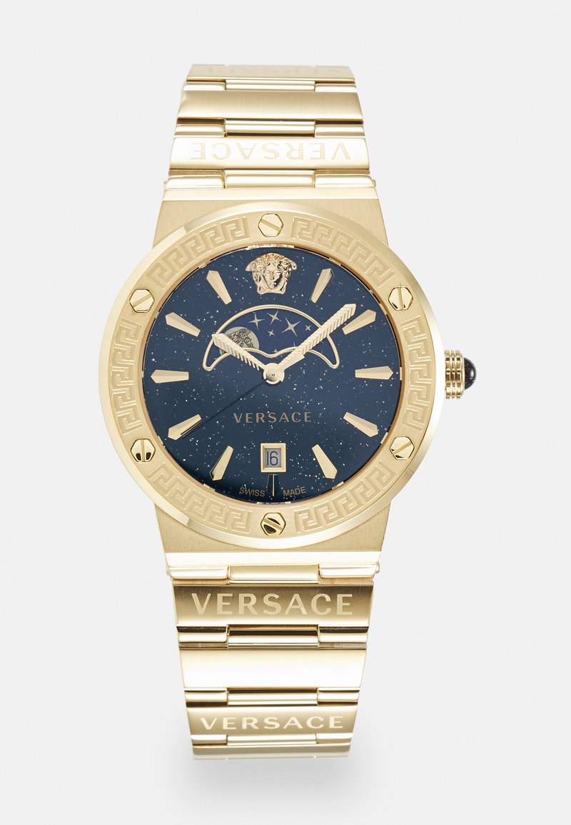 Auksinės spalvos Versace laikrodis su tamsiai mėlynu dėklu, išmargintu taškeliais, Graikijos rakto rašto įrėminimu ir masyvia grandinės juosta su prekės ženklu. Taip pat yra datos rodymas.