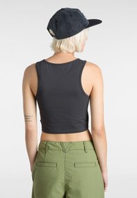 Grå kortärmad crop top av slät tyg, kombinerad med olivgröna byxor med bakfickor och stickningsdetaljer.