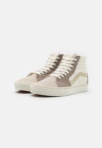 Zapatillas altas con paneles de ante beige y marrón claro, detalles de lienzo blanco y cordones blancos, con una suela de goma texturizada.