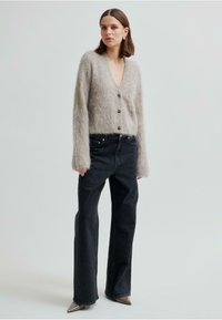 Ljusgrått, lurvigt cardigan med djup V-urringning, långa ärmar och mörka knappar, kombinerat med svarta jeans och spetsiga beige klackskor.