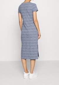 Robe midi rayée gris avec des manches courtes, un col rond, des fentes sur les côtés et une texture douce. Associée à des baskets blanches.