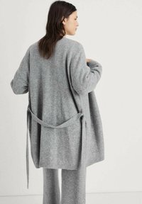 Cardigan grigio lavorato a maglia con un fit rilassato, legato in vita con una cintura. Il tessuto ha una finitura morbida e testurizzata e polsini a coste.