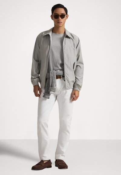 Ανοιχτό γκρι μπουφάν με φερμουάρ πάνω από γκρι μπλουζάκι, λευκό παντελόνι και καφέ μοκασίνια. Ένα γκρι πλεκτό είδος είναι δεμένο γύρω από τη μέση. Φοράει σκουρόχρωμα γυαλιά ηλίου.