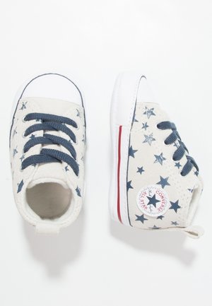 Białe dziecięce trampki z niebieskimi wzorami gwiazdek, granatowymi sznurowadłami i podeszwą w czerwone paski, widoczne z góry i z boku.