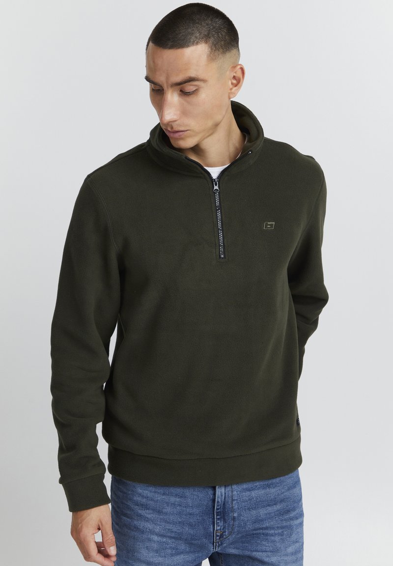 Pullover in pile verde scuro con collo alto, chiusura a zip quarti e discreto dettaglio del logo sul petto. Texture morbida e vestibilità comoda.
