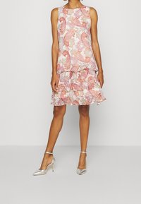 Ermeløs kjole med et lagdelt flæse skørt i et pink og flerfarvet paisley mønster, lavet af letvægtsstof. Sølv høje hæle.