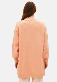 Pfirsichfarbener, oversized Pullover mit hohem Kragen, gerippten Bündchen und Saum; weiche Textur; von hinten gezeigt.