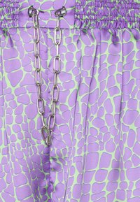 Violetti ja vihreäkuvioitu kangas, jossa on smokkivyötärö ja hopeaketjuyksityiskohta. Sileä pinta, jossa epäsäännöllisiä geometrisia muotoja.