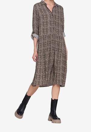 Woman wearing a brown and black snake-print midi dress with rolled sleeves and black chunky boots with beige soles.