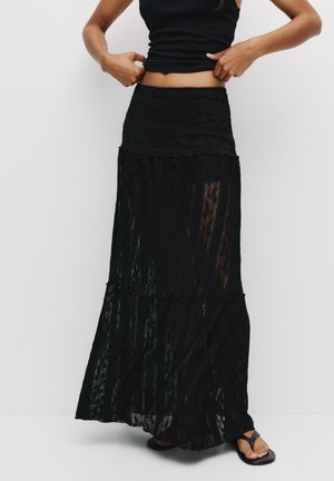 Fustă maxi din dantelă neagră, cu un design în straturi, având o talie ajustată și o textură transparentă. Purtați-o cu un top negru și sandale.