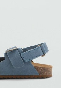 Sandalo blu scamosciato con una larga cintura, fibbia regolabile e suola in sughero marrone testurizzato. Forma arrotondata con una base piatta per stabilità.