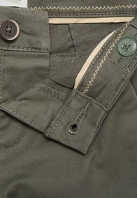 Pantaloni de culoare verde măsliniu, cu un finisaj neted și texturat. Au un sistem de închidere cu buton și detalii de cusătură contrastantă pe talie.