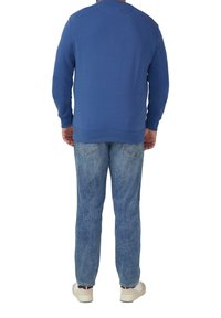 Felpa blu con scollo rotondo, maniche lunghe e polsini a coste, abbinata a jeans in denim azzurro chiaro. Mostrati anche scarpe da ginnastica chiare.