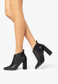 Bottines noires aux orteils pointus, avec des talons blocs texturés, des zips sur le côté et un mélange de matériaux lisses et à motifs.