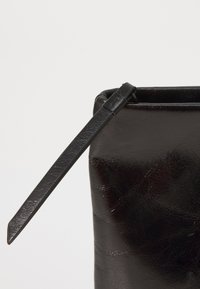Borsa a pochette in pelle nera caratterizzata da un design elegante, una texture liscia e una tracolla sottile attaccata a un'apertura superiore sicura.