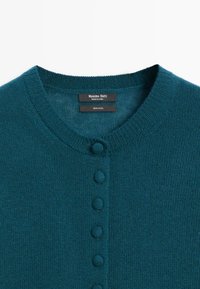 Cardigan in lana color teal, con scollo rotondo, chiusura frontale con bottoni testurizzati e polsini e orlo a coste.