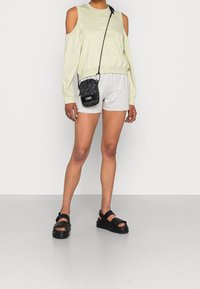 Helle grüne Sweatshirt mit kaltem Schulterdesign, kombiniert mit grauen Shorts. Das Accessoire umfasst eine kleine schwarze Tasche mit Leopardenmuster. Schwarze Sandalen.