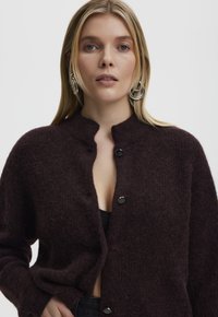 Dark brown, fuzzy cardigan with a stand-up collar, two black buttons, and relaxed fit. Textured fabric with visible fibers.