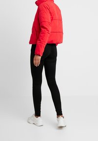 Czerwona kurtka puchowa o skróconym fasonie, teksturowana tkanina i kieszenie na zamek, w połączeniu z czarnymi spodniami slim fit i białymi sneakerami.