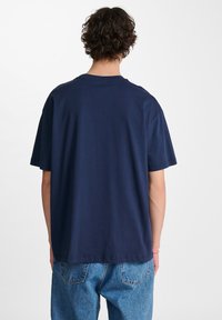 Marinblå bomullströja med korta ärmar, rund hals och avslappnad passform. Inga synliga grafiker eller mönster. Bakvy visas.