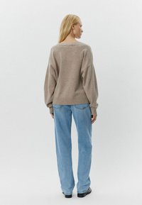 Pulover tricotat bej cu gât larg și mansete cu dungi, asortat cu blugi drepti de culoare bleu deschis și pantofi negri, văzut din spate.