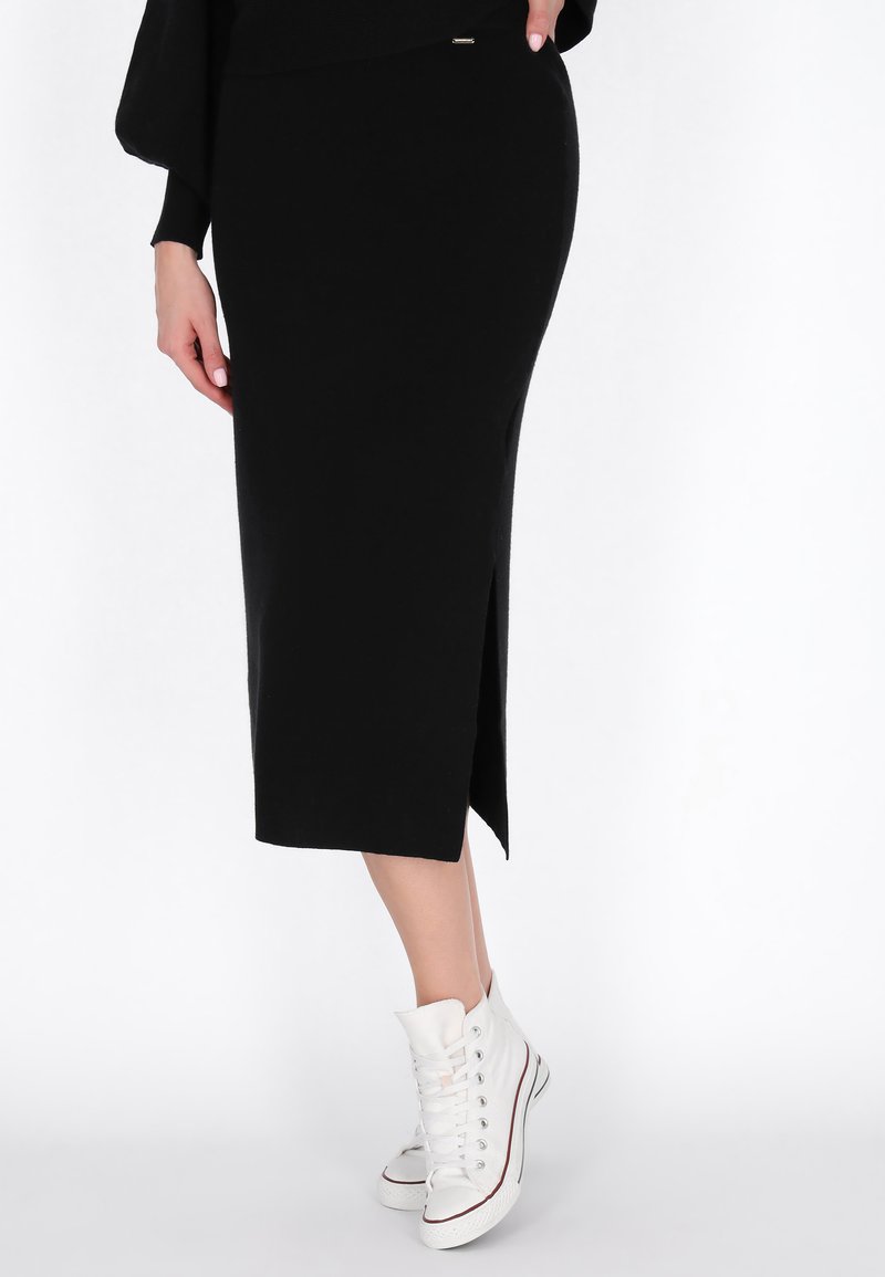 Černá midi sukně se bočním rozparkem, vyrobená z měkké látky. V kombinaci s bílými botami na vysoké podešvi. Jednoduchý, elegantní design. Žádné viditelné vzory.